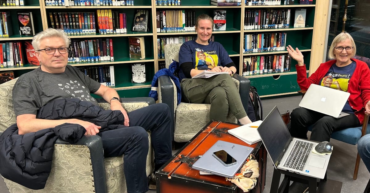 Tre personer sitter med pc-er på et bibliotek.